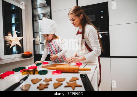 A heartwarming scene of a cheerful mother and her daughter joyfully baking festive cookies together in the kitchen Stock Photo
