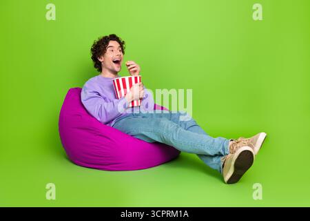 Young man enjoys popcorn while seated comfortably on a colorful bean bag resembling relaxation in style Stock Photo