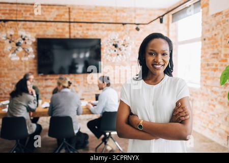 Portrait of smiling young female business expert standing with arms crossed in office Stock Photo