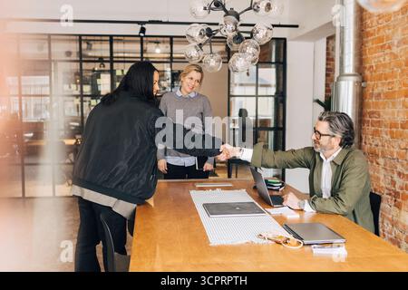 Happy woman shaking hands with male recruiter sitting at table for job interview in office Stock Photo