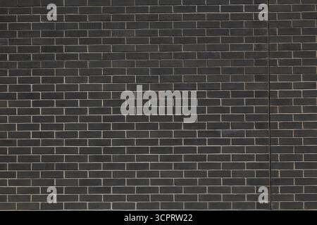 Exterior wall of building composed of dark grey rectangular shape clay bricks with light grey mortar joints. Stock Photo
