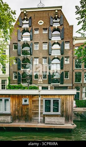Iconic home= with black shutters  on a canal with a houseboat n Amsterdam, Netherlands Stock Photo