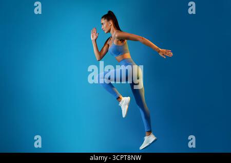 Sporty Woman Exercising Doing Elbow-To-Knee Crunch Standing On Blue Background Stock Photo