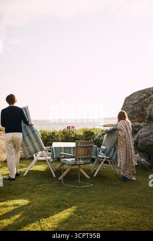 Man and woman keeping mattresses on chair while preparing for dinner party in back yard Stock Photo