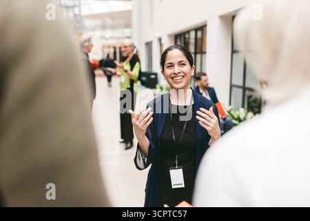 Happy female business entrepreneur gesturing while talking with colleagues in congress center Stock Photo