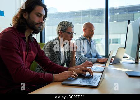 Three multiracial business colleagues sitting in the office working using laptops. Stock Photo