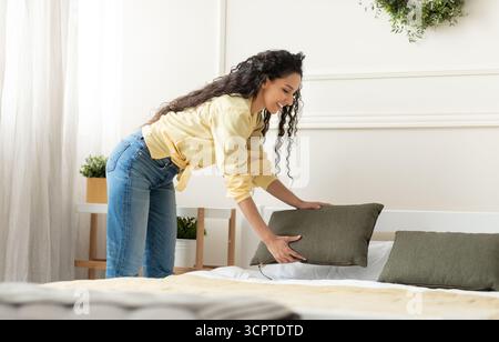 Portrait of cheerful young woman making bed after wake up Stock Photo