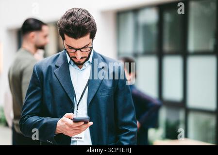 Focused male business expert using smart phone while standing in convention center Stock Photo