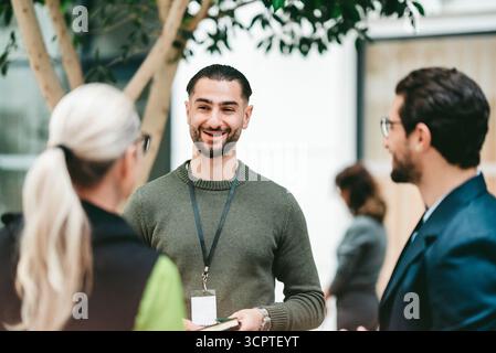 Happy young male business professional standing with coworkers in convention center Stock Photo