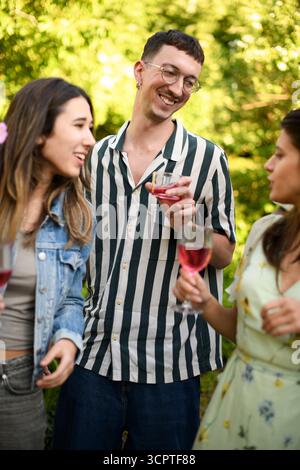 Smiling young man enjoying red wine with female friends at social gathering in back yard Stock Photo