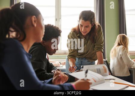 Female professor assisting male student studying in classroom at junior high school Stock Photo