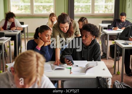 Female teacher assisting junior high students using calculator for math problem in classroom at school Stock Photo
