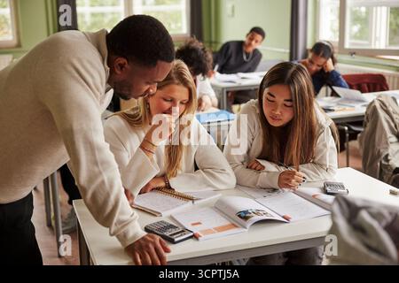 Male teacher discussing math equations with female students in classroom at junior high school Stock Photo