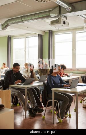 Female teacher assisting students doing e-learning in classroom at junior high school Stock Photo