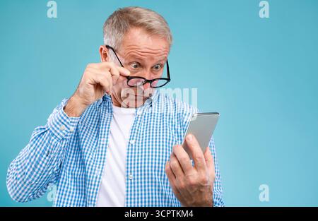 Surprised mature man using mobile phone, looking at screen Stock Photo