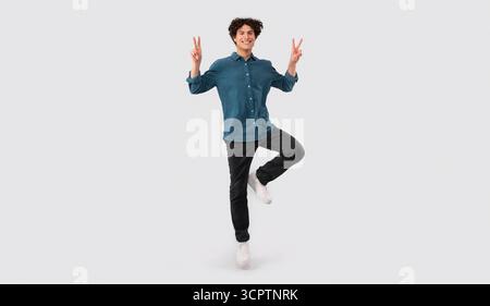 Young Brunette Man Gesturing V Sign Over Light Gray Background Stock Photo