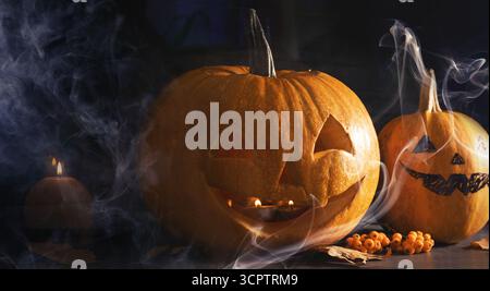 Halloween celebration. Pumpkins with carved spooky faces and smoke in darkness Stock Photo
