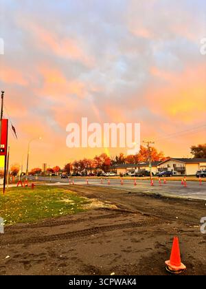 Rainbow over a road construction site at sunset, with orange cones and houses under a colourful sky. Stock Photo