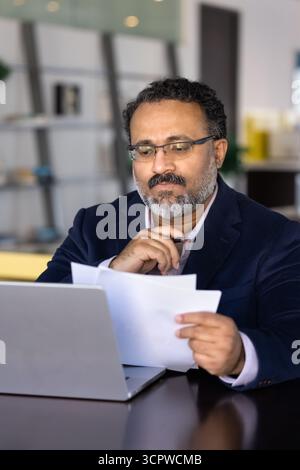 Focused businessman carefully reading printed documents while sitting at desk Stock Photo