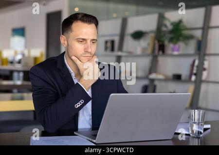 Professional businessman looking at laptop screen with pensive expression Stock Photo
