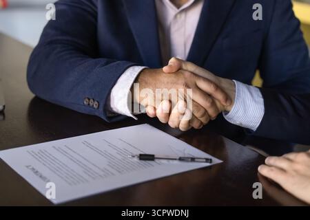 Two business professionals firmly shaking hands over signed contract Stock Photo