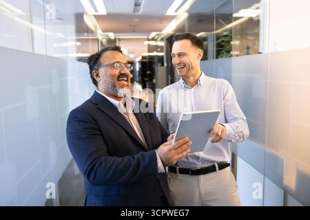 Two businessmen laughing, discussing work-related matters or content on tablet Stock Photo