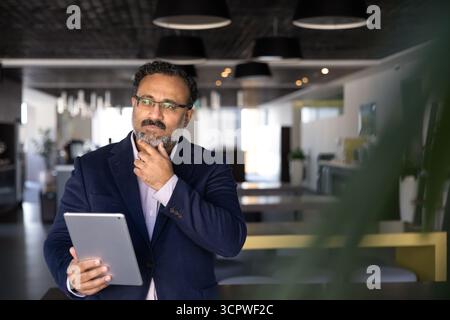 Indian man analyzing information on tablet working in coworking office Stock Photo
