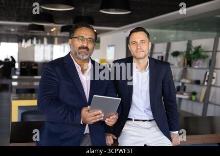Two confident businessmen in suits posing together in modern office Stock Photo