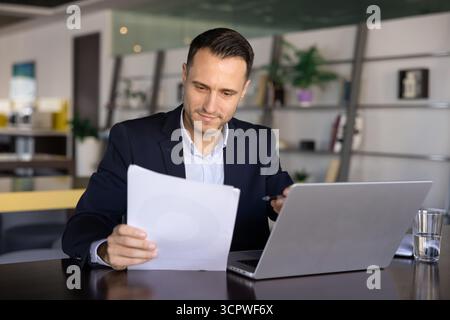 Businessman reviewing printed documents while working on laptop Stock Photo