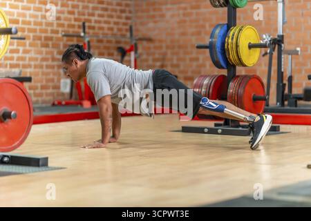 Athlete with prosthetic leg doing push ups on a gym floor, showcasing adaptive strength training, determination and focused bodyweight workout for reh Stock Photo