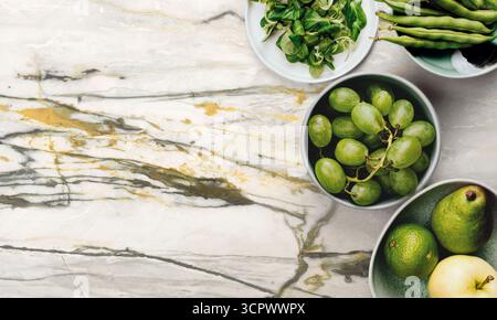 Fresh green vegetables and juicy fruits arranged on a marble surface for healthy cooking inspiration. Stock Photo