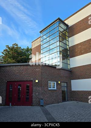 brick and white school building featuring a red door and a tall glass stairwell, blending modern design with functional architecture Stock Photo