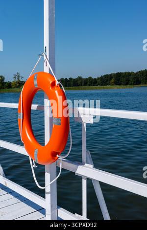 Orange swimming rescue wheel hanged on the rails of the white jetty ...
