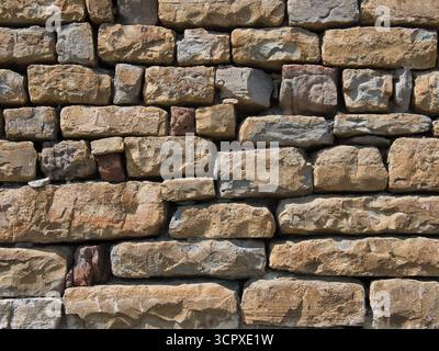 Rough Cut Random Pattern Stone Wall Texture - Close-up of a weathered, rustic stone wall made of rough-cut rectangular blocks in varying shades of tan Stock Photo