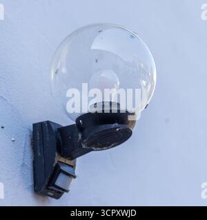 Close-up of a round outdoor light fixture with a motion sensor, mounted on a textured white wall. Stock Photo