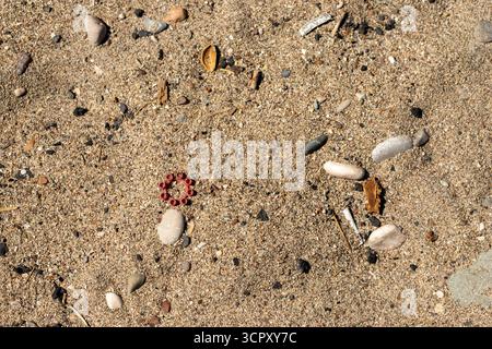 Overhead shot of tan sand with small pebbles, debris, and a red plastic toy ring. Stock Photo