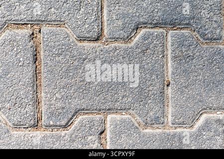 Close-up of gray concrete pavers with interlocking design, separated by sand or dirt filled seams. Stock Photo