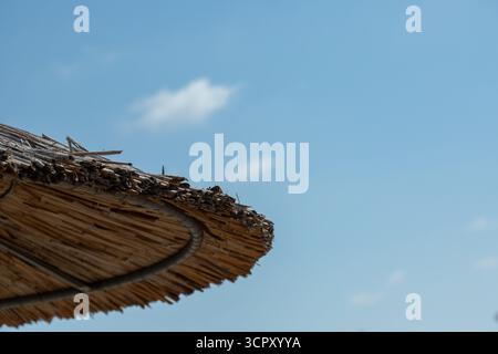 A close-up of a thatched umbrella against a blue sky. The umbrella is the dominant feature, with the sky providing a simple background. Stock Photo