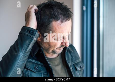 Mature adult man scratching his head and squinting, looking confused or forgetful, concept of memory loss, doubt, stress, or difficulty concentrating. Stock Photo