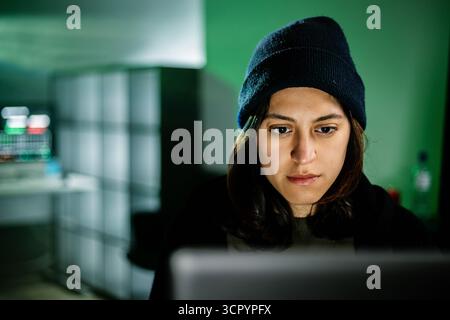 Female young hacker working on computer in dark room programming code Stock Photo