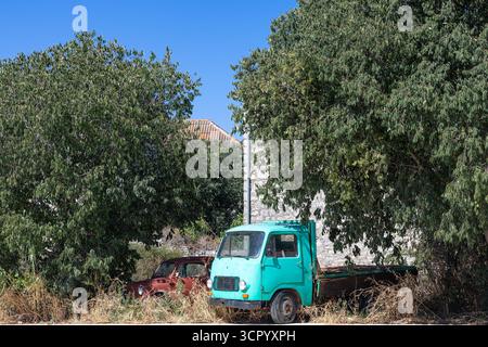 A vintage turquoise truck rests in a sunlit rural setting, framed by lush trees and an old stone wall. Abandoned and nostalgic, the scene conveys quie Stock Photo