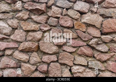 A cobblestone wall made of stones of various sizes and shapes. Stone wall texture. A natural stone wall as a background. Stock Photo