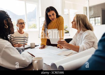 Diverse group of professional women architects of varying ages working together on a design project in a bright office setting, demonstrating collabor Stock Photo
