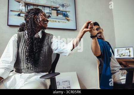 Two architects, a young man and a woman, exchange a high five while working on a project in a modern office. They express teamwork, success, and colla Stock Photo