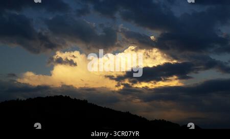 Dramatic evening sky with strong contrasts of bright white clouds illuminated by the sun and surrounded by dark, almost black clouds Stock Photo