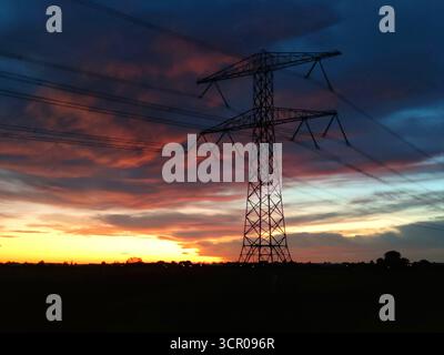 Ecololectricity pylon standing tall against a colorful sunrise sky over the quiet countryside Stock Photo