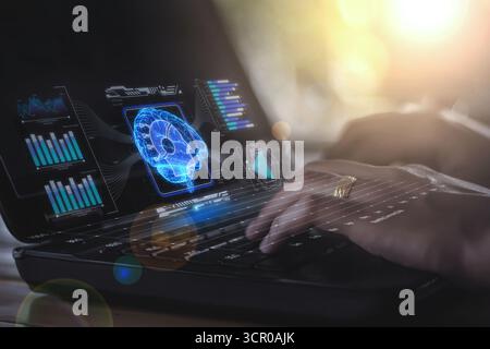 A network graph connected to a hologram of a brain, surrounded by glowing blue lines, floats on the screen of a computer that a businesswoman is using Stock Photo