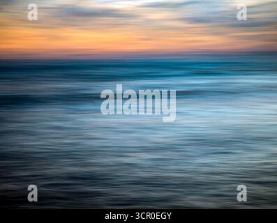 Colors blend beautifully as the sun sets over the Atlantic Ocean in Huelva, Spain. Long exposure captures the motion of waves and sky. Stock Photo