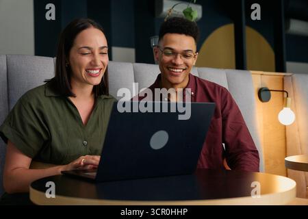 Smiling diverse young business people in smart casual discussing over laptop at desk in office Stock Photo