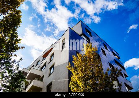 Modern residential building with reflective blue facade and geometric design under cloudy sky with bright light Stock Photo